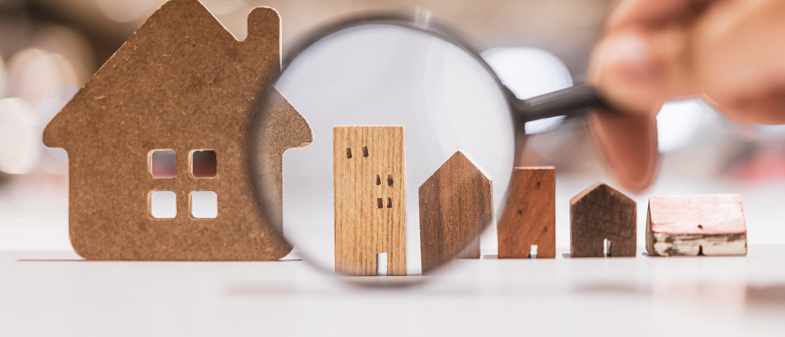 Handholdingmagnifyingglassandlookingathousemodelhouseselectionrealestateconcept.
